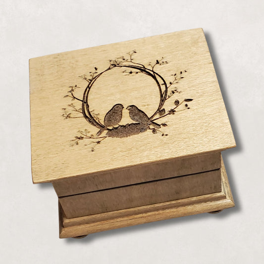 Wooden music box with an oval floral engraved design of two birds sitting on a nest inside