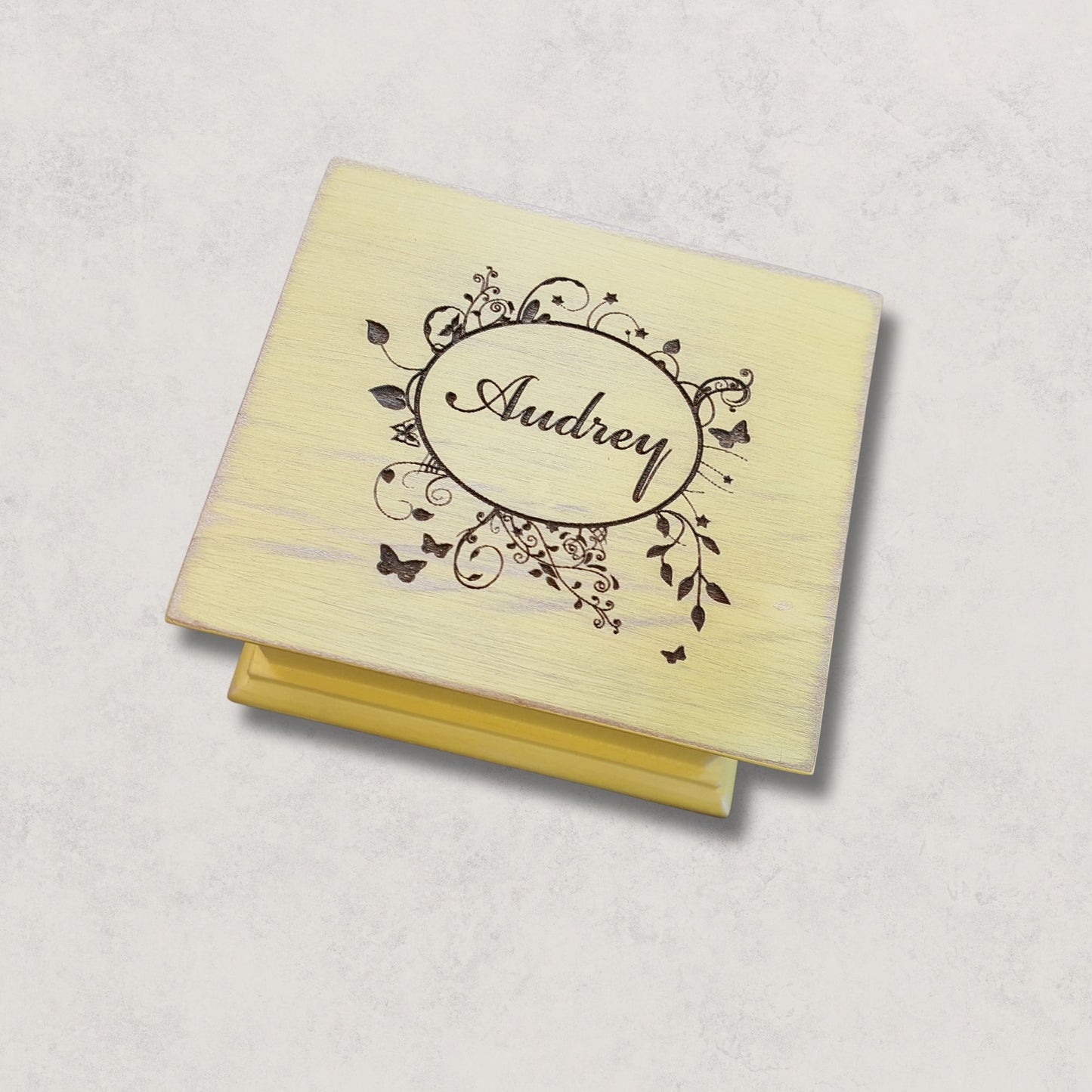 Wooden music box with 'Audrey' engraving in an oval floral frame on a light gray background