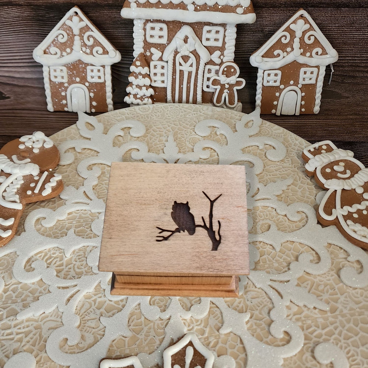 Wooden box with owl design on a decorative surface with gingerbread houses.