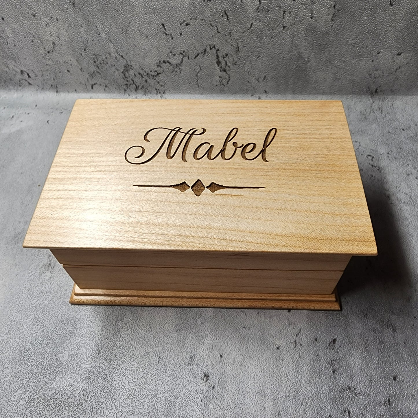 wooden jewelry box with a name engraved on it with a beautiful script font, and a decorative underline. it plays your song in music box sound when you open it, and you can choose the color and add a personalized message to the bottom side of box