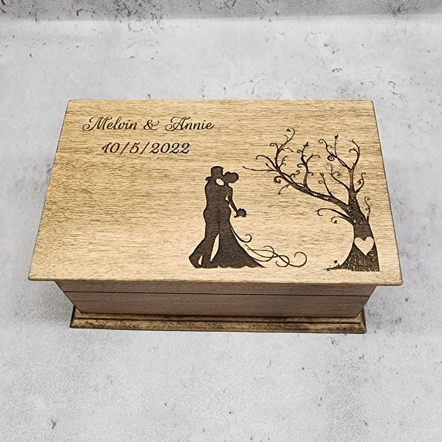 A wooden jewelry box with a couple and a tree engraved on the lid, with personalized text including names and a date. choose from 9 colors, add personalized message