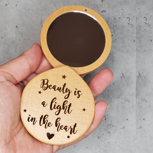 Wooden pocket mirror engraved with an inspirational quote saying Beauty is a light in the heart